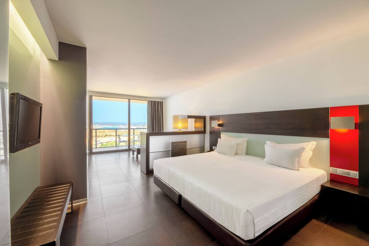 A hotel room with a large bed, a TV, a desk, and a view of the outdoors.
