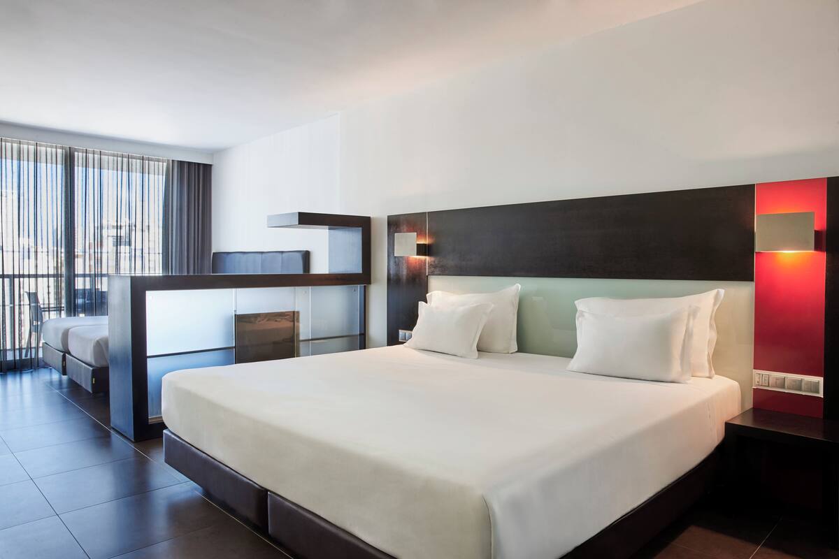 A modern hotel room with a large bed, a desk, and a balcony with curtains.