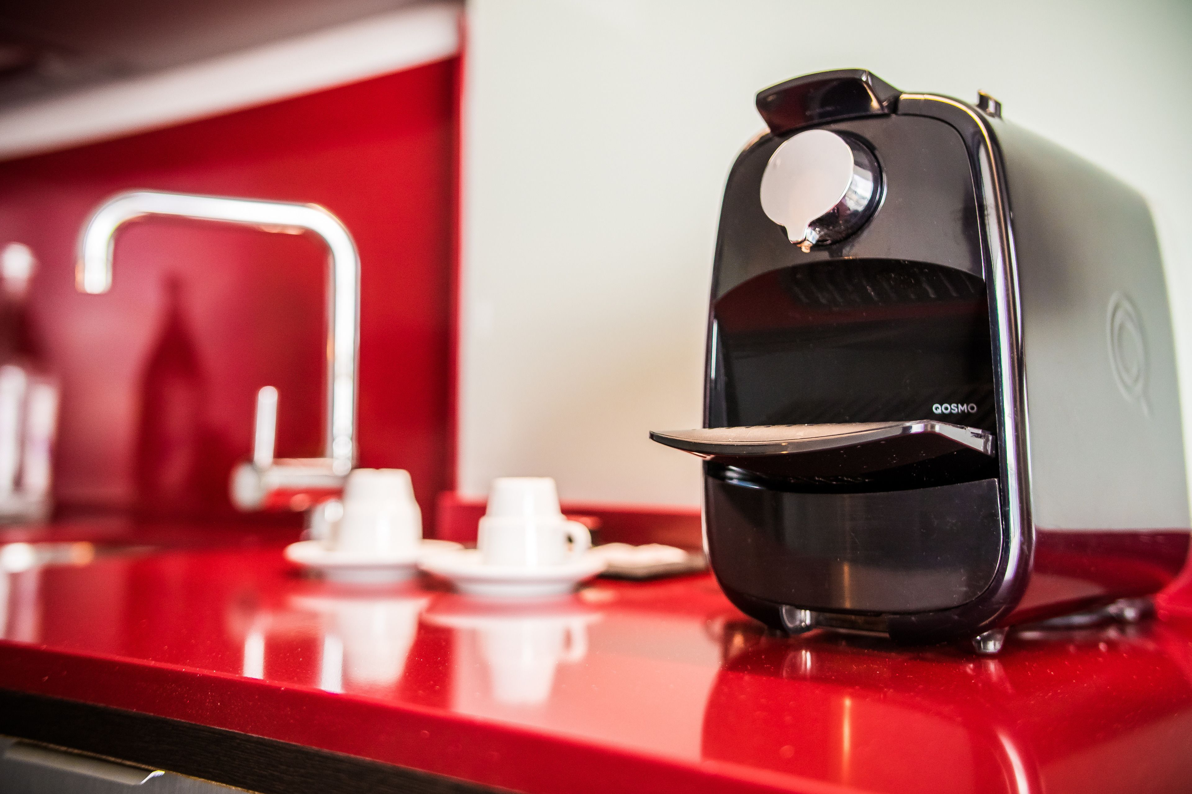 A coffee machine on a red countertop with a white cup and saucer nearby.