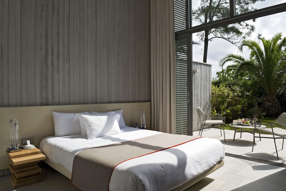 Ein modernes Hotelzimmer mit einem großen Bett, einem Nachttisch mit Lampe und Blick auf die Außenpatio-Terrasse.