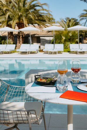 Une table placée au bord de la piscine, avec deux verres de vin, un saladier de fruits et une chaise.