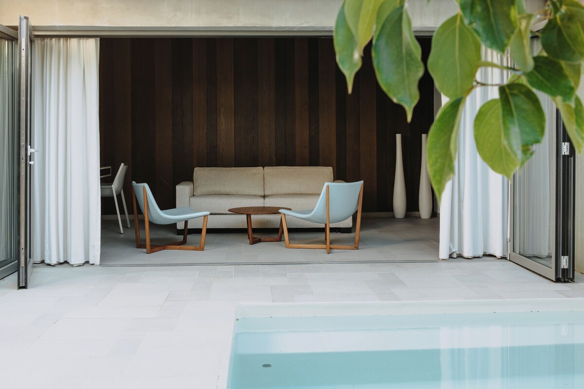 Un espace piscine intérieur comprenant un canapé, deux fauteuils, une petite table et une plante en pot.