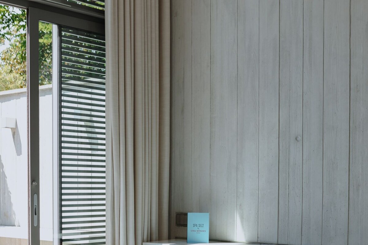 Une pièce moderne avec une porte en verre, deux chaises bleu clair, une petite table ronde et un tapis rouge.