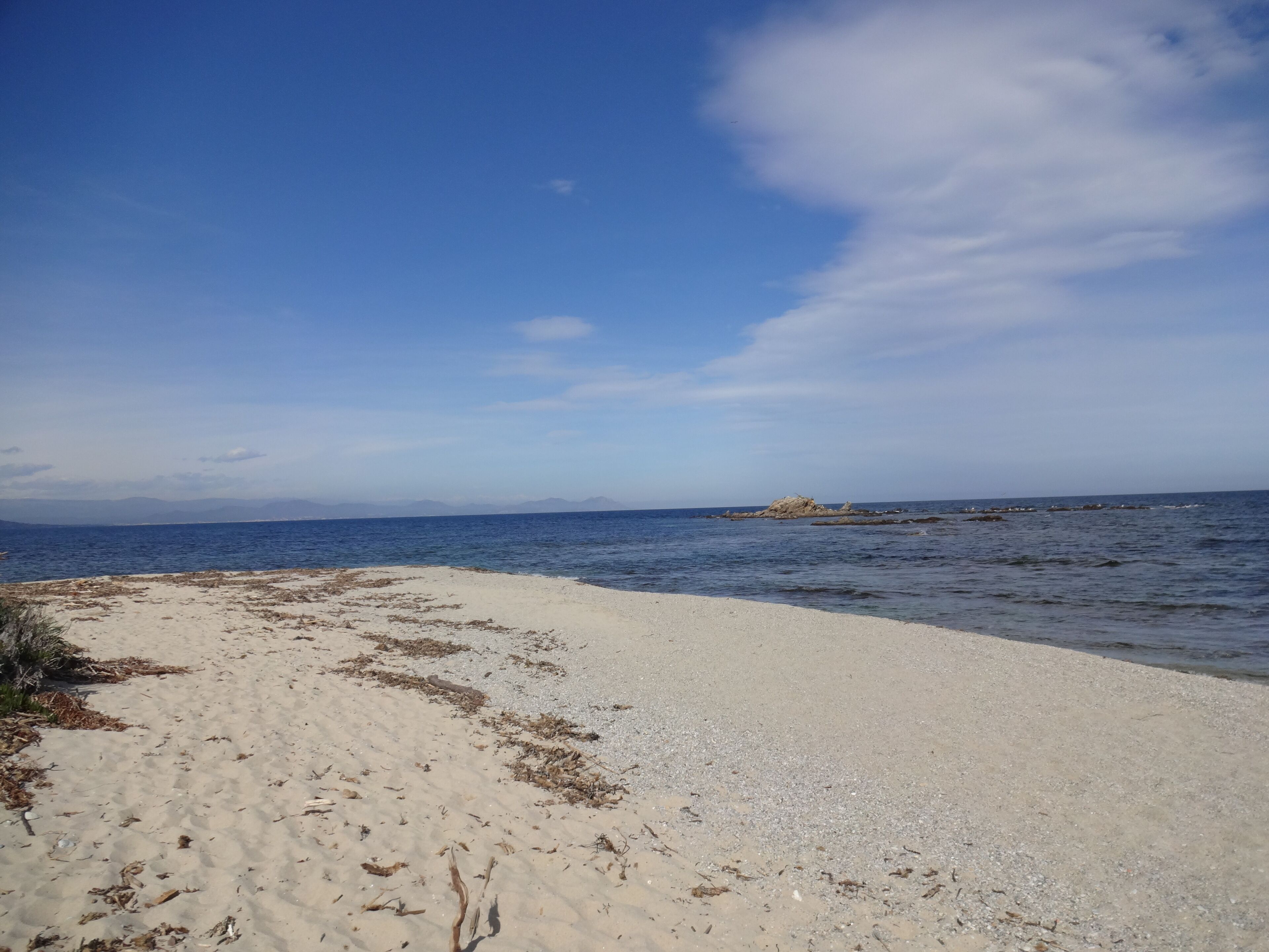 Une plage avec un ciel dégagé, une mer calme et des affleurements rocheux.