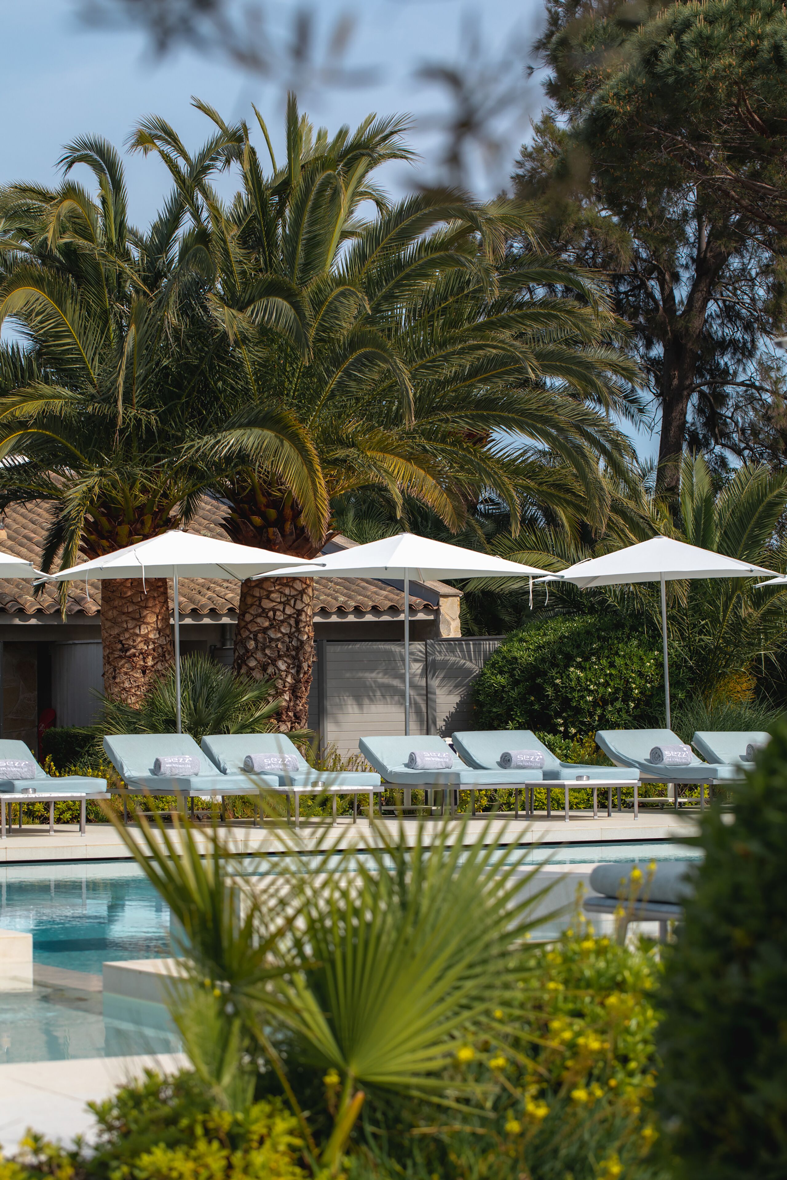 A pool area with lounge chairs and umbrellas, surrounded by palm trees and a stone building.