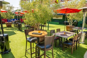 An outdoor patio with round tables and chairs, surrounded by greenery and umbrellas.
