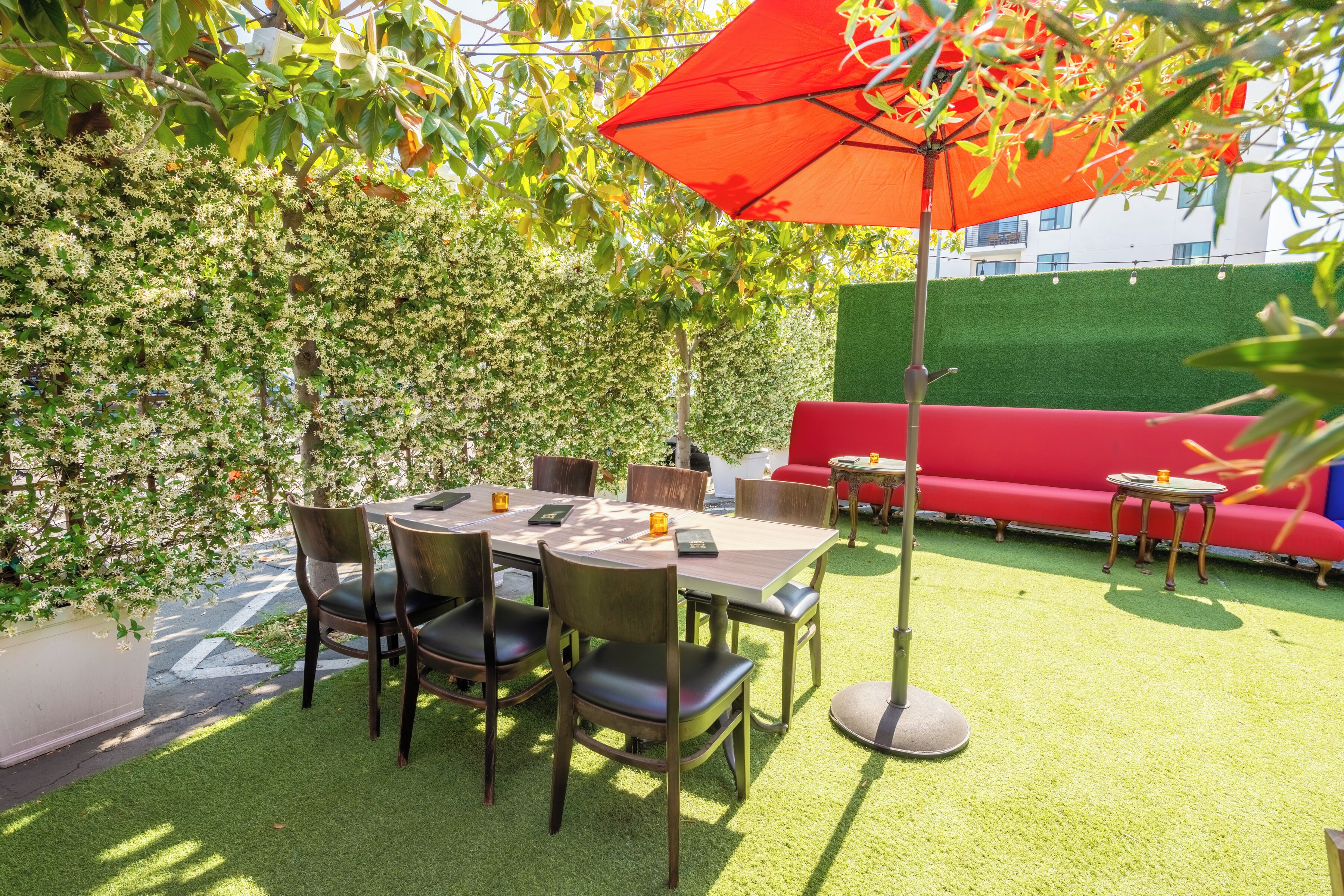 An outdoor seating area with a table and chairs, a red sofa, and an orange umbrella.