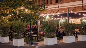 An outdoor seating area with tables and chairs, surrounded by potted plants, under string lights.