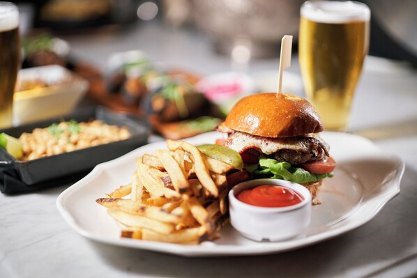 A plate with a burger, fries, and ketchup, and a glass of beer.