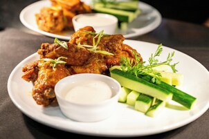 Un plato de alitas de pollo con pepino y un recipiente pequeño de salsa.