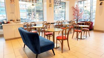 A cafe with multiple tables and chairs, large windows, and a view of the street outside.