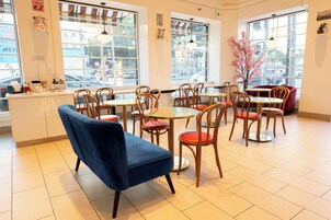 Een café met meerdere tafels en stoelen, grote ramen en uitzicht op de straat.