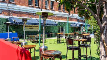 An outdoor seating area with tables and chairs, a red sofa, and a building with a green awning in the background.