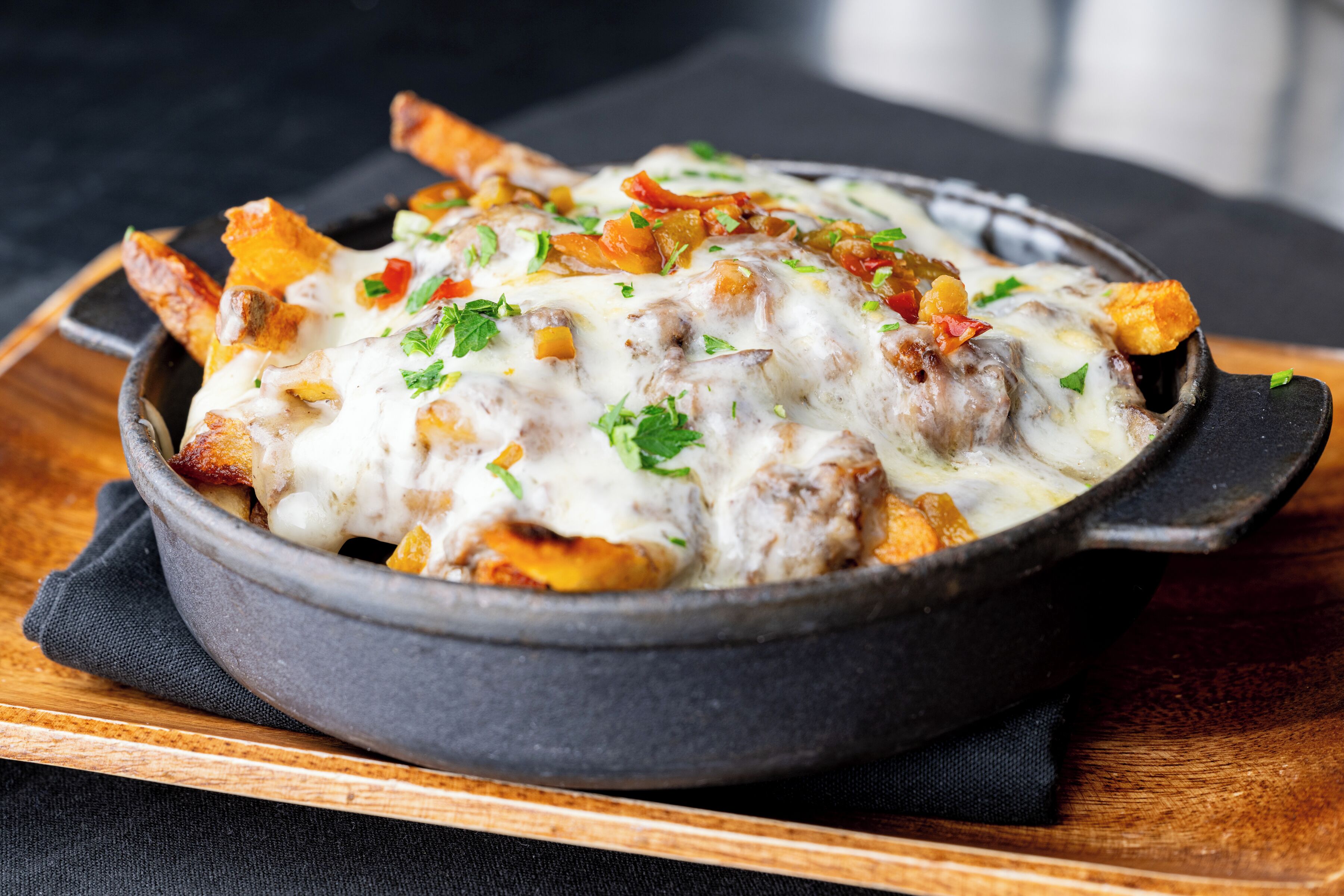 A skillet with a dish of fries topped with melted cheese and garnished with herbs.