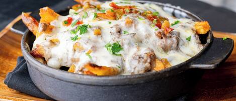 A skillet with a dish of fries topped with melted cheese and garnished with herbs.