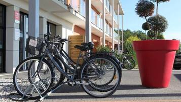 Cyklar parkerade framför en byggnad med en stor, röd blomlåda och ett trästaket.