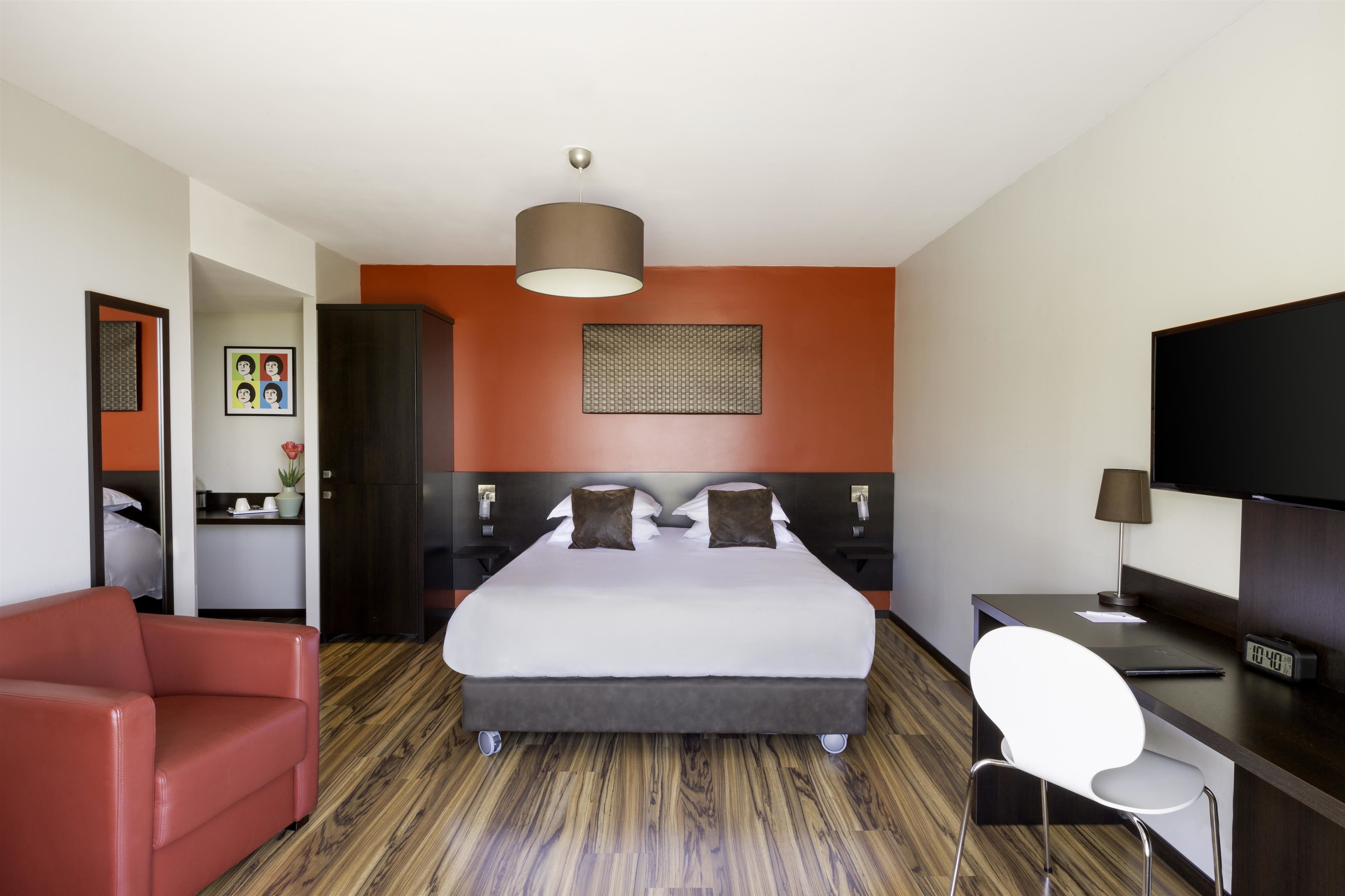 A hotel room with a large bed, a desk with a chair, a TV, and a red sofa.