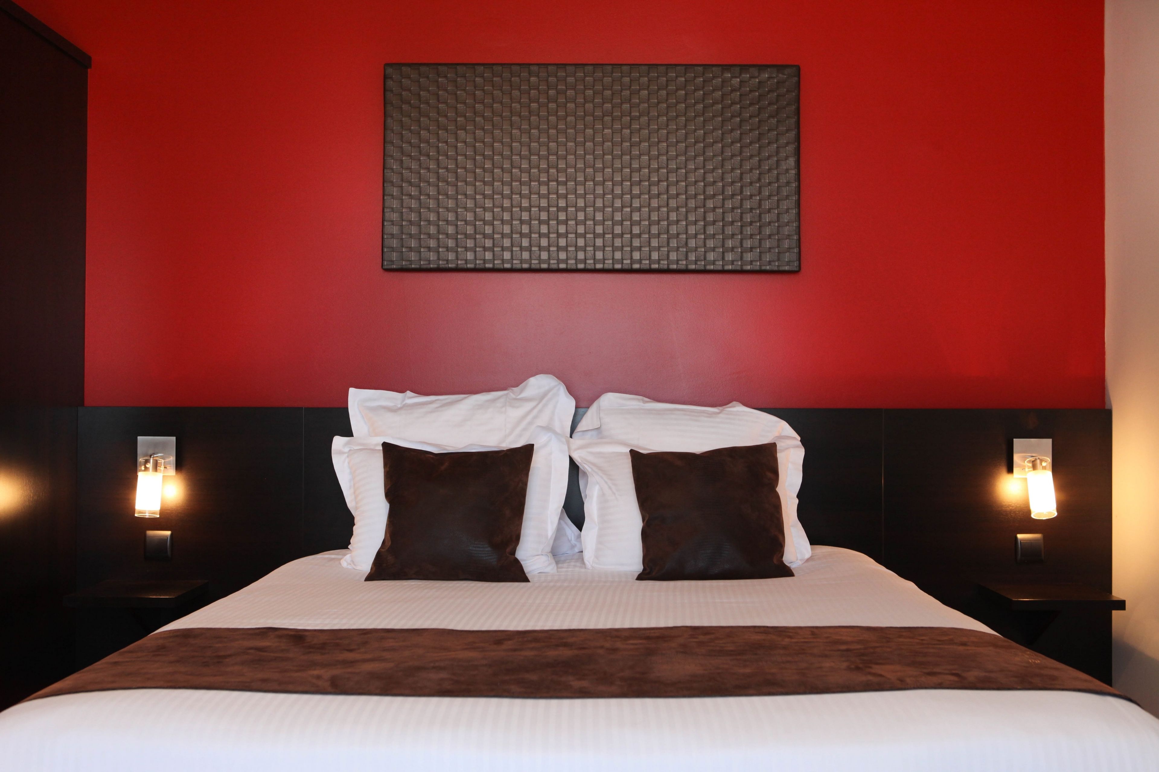 A hotel room with a large bed, two bedside tables, and a red accent wall.