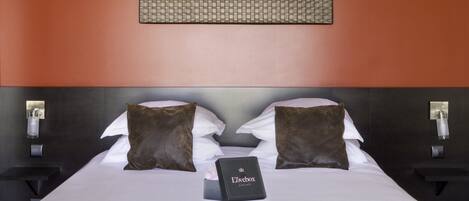 A neatly made bed with a white comforter, two brown pillows, and a small black box labeled "Lovebox" on the bed.