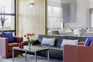 Um hall de hotel moderno com sofás de couro, uma mesa de centro e uma grande janela.