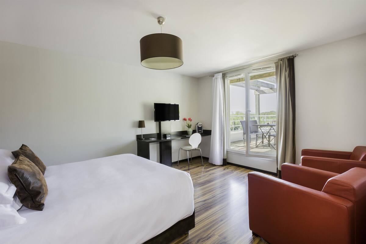A hotel room with a bed, a desk, a chair, and a sofa.