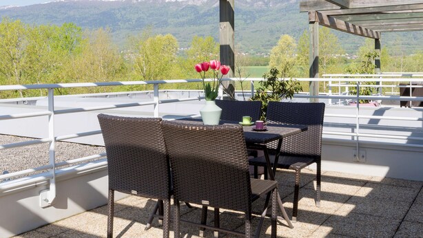 A terrace with wicker chairs and a table, a vase with flowers, and a view of snow-capped mountains. - Best Western Park Hotel Geneve-Thoiry (Thoiry)