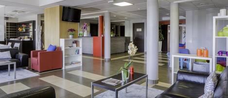 Un hall d’entrée moderne avec un comptoir d’accueil, des espaces détente et un téléviseur fixé au mur.