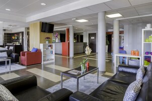 Um lobby moderno com balcão de recepção, áreas de estar e uma TV fixada na parede.