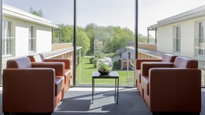 A modern hotel room with a large window, a small table with a decorative glass vase, and two leather sofas. - Best Western Park Hotel Geneve-Thoiry (Thoiry)
