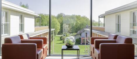 A modern hotel room with a large window, a small table with a decorative glass vase, and two leather sofas.