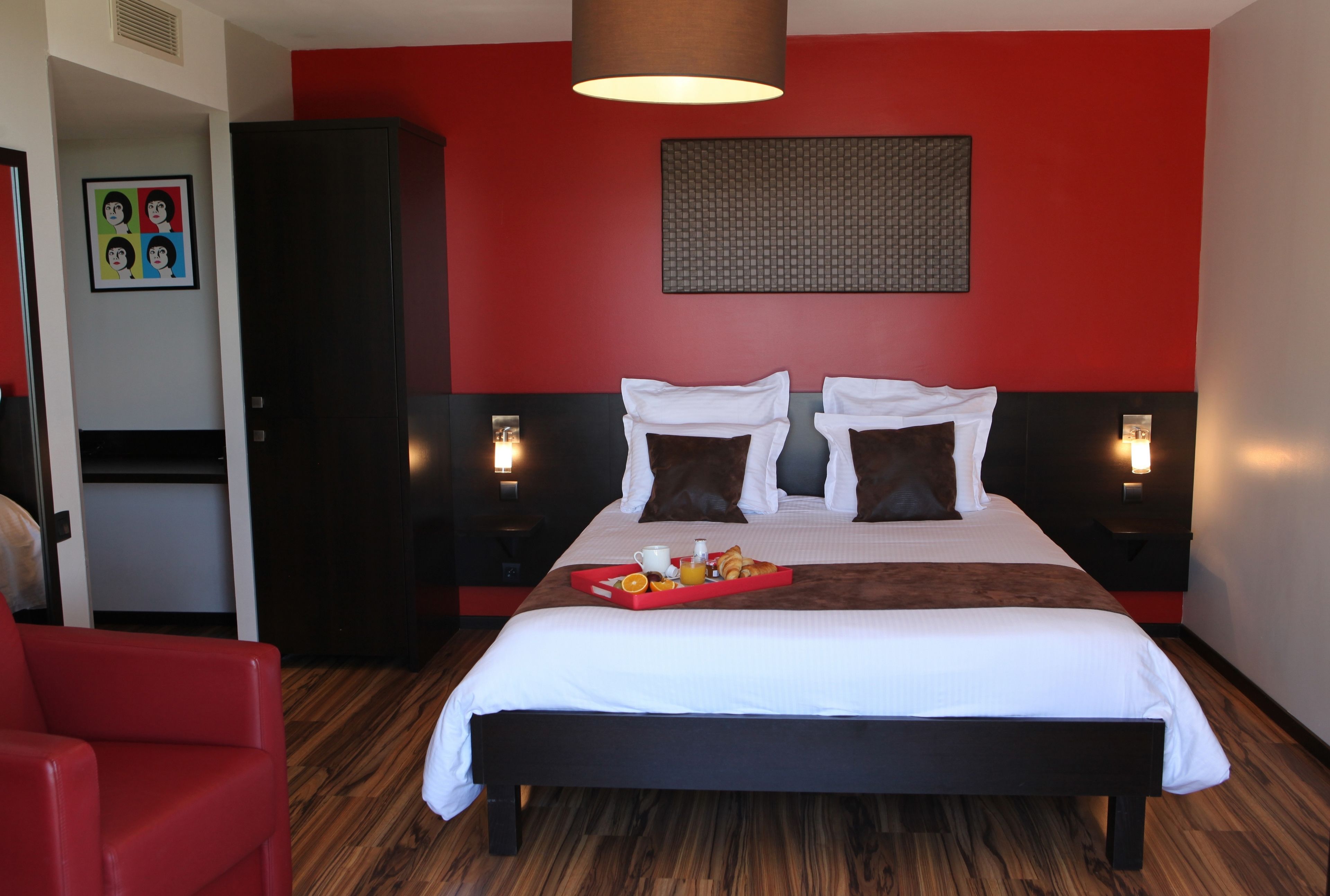 Una habitación de hotel con una cama grande, paredes rojas, suelo de madera y un sillón rojo.