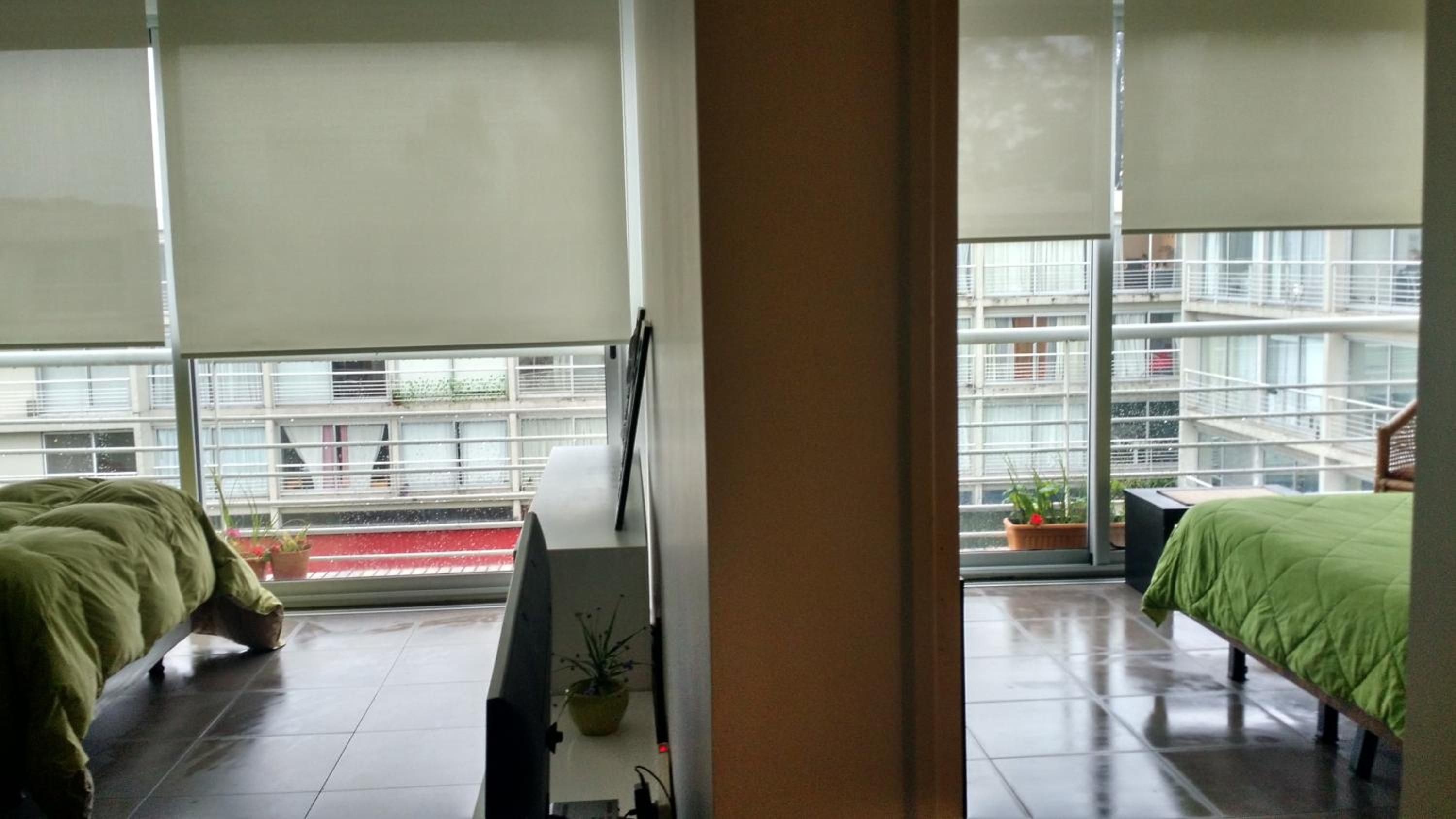 Habitación de hotel moderna con un ventanal grande, una cama, una mesita de noche y vistas a la ciudad.