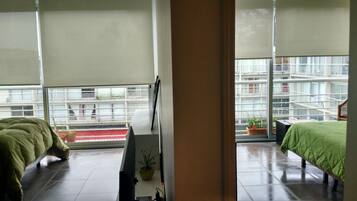 Habitación de hotel moderna con un ventanal grande, una cama, una mesita de noche y vistas a la ciudad.