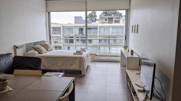 A modern hotel room with a bed, a sofa, a TV, and a balcony with a view of buildings. - Concord Pilar Apart Suite 313 - Almendros (La Lonja)