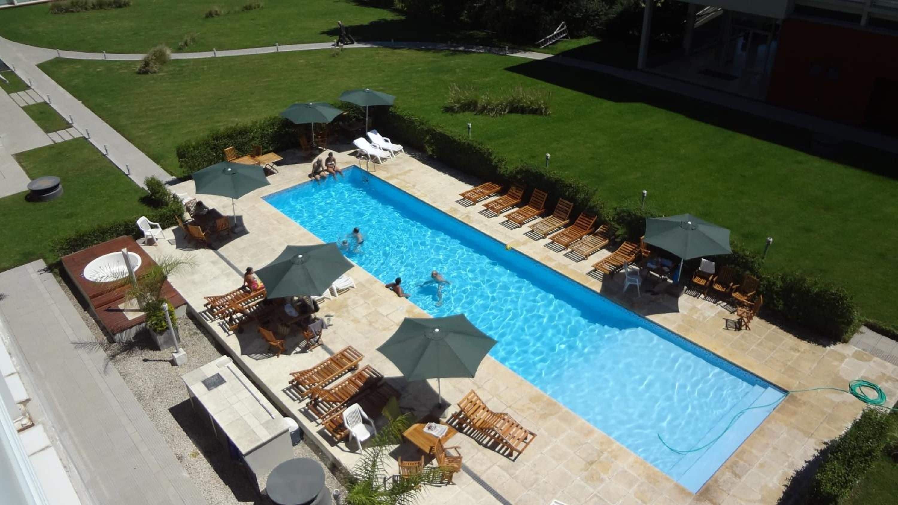 Una piscina rectangular con sillas de descanso y sombrillas, rodeada de un césped cuidado y un camino pavimentado.