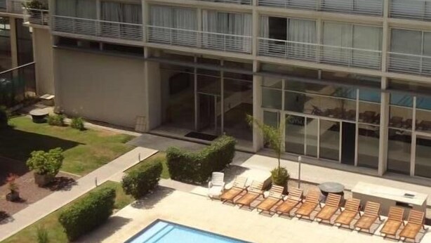 A multi-story hotel with a rooftop pool area, outdoor seating, and a well-maintained garden.