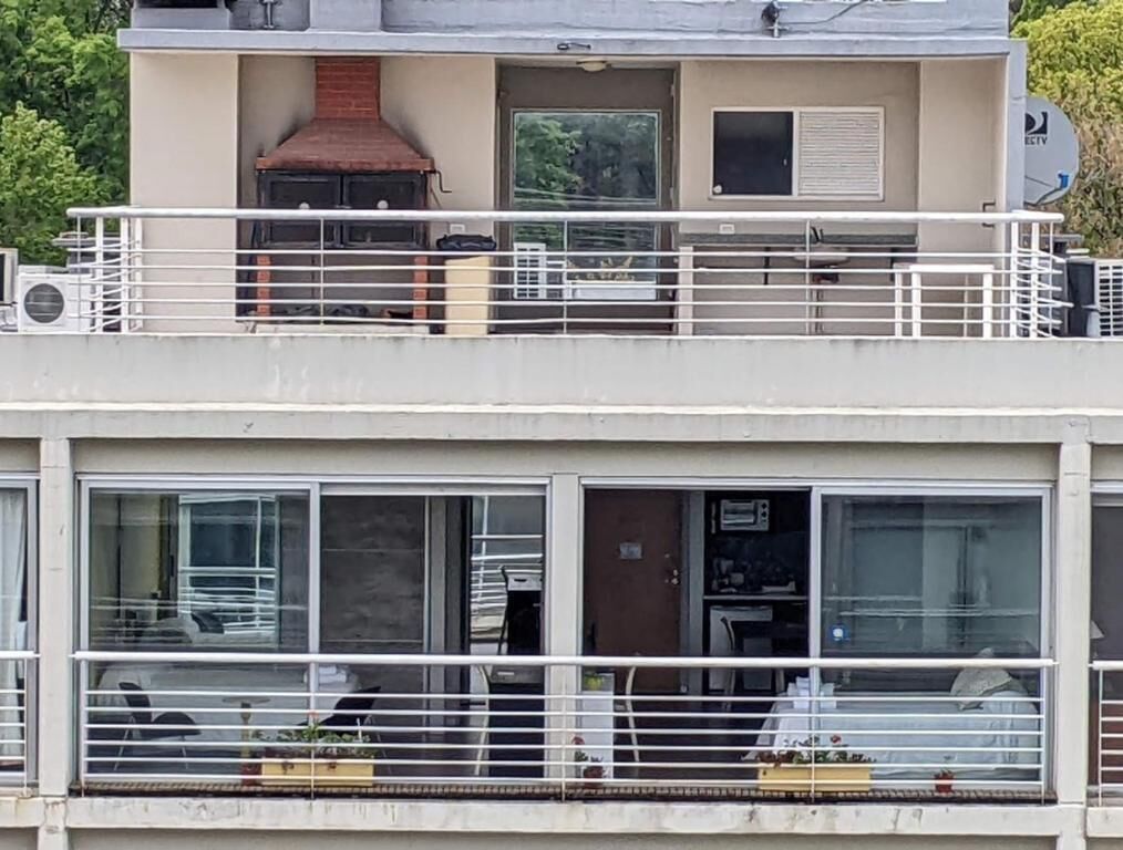 Un edificio de dos pisos con balcón, ventanas grandes y chimenea.