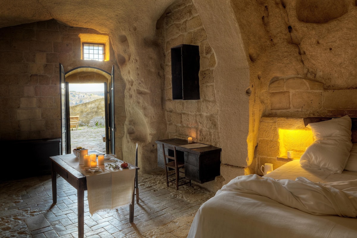 Une pièce rustique aux murs de pierre, avec un lit, un bureau et une petite table décorée de bougies.