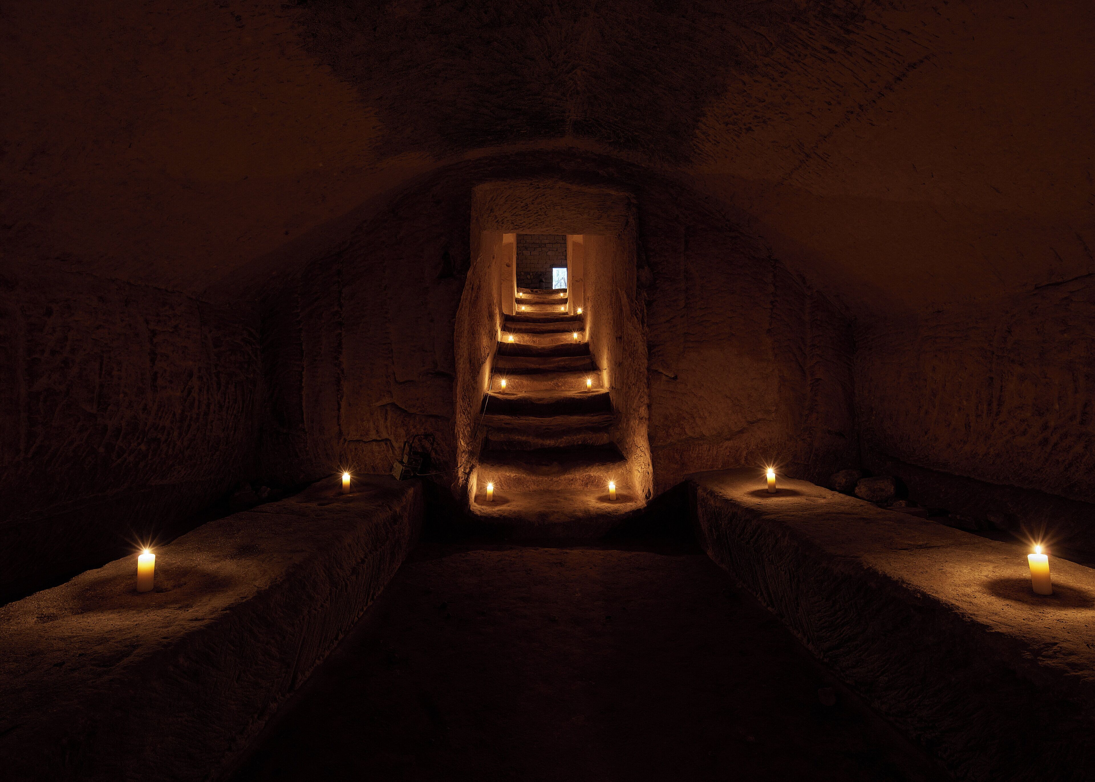 A dimly lit stone staircase leading to a higher level, with candles placed at intervals along the sides.