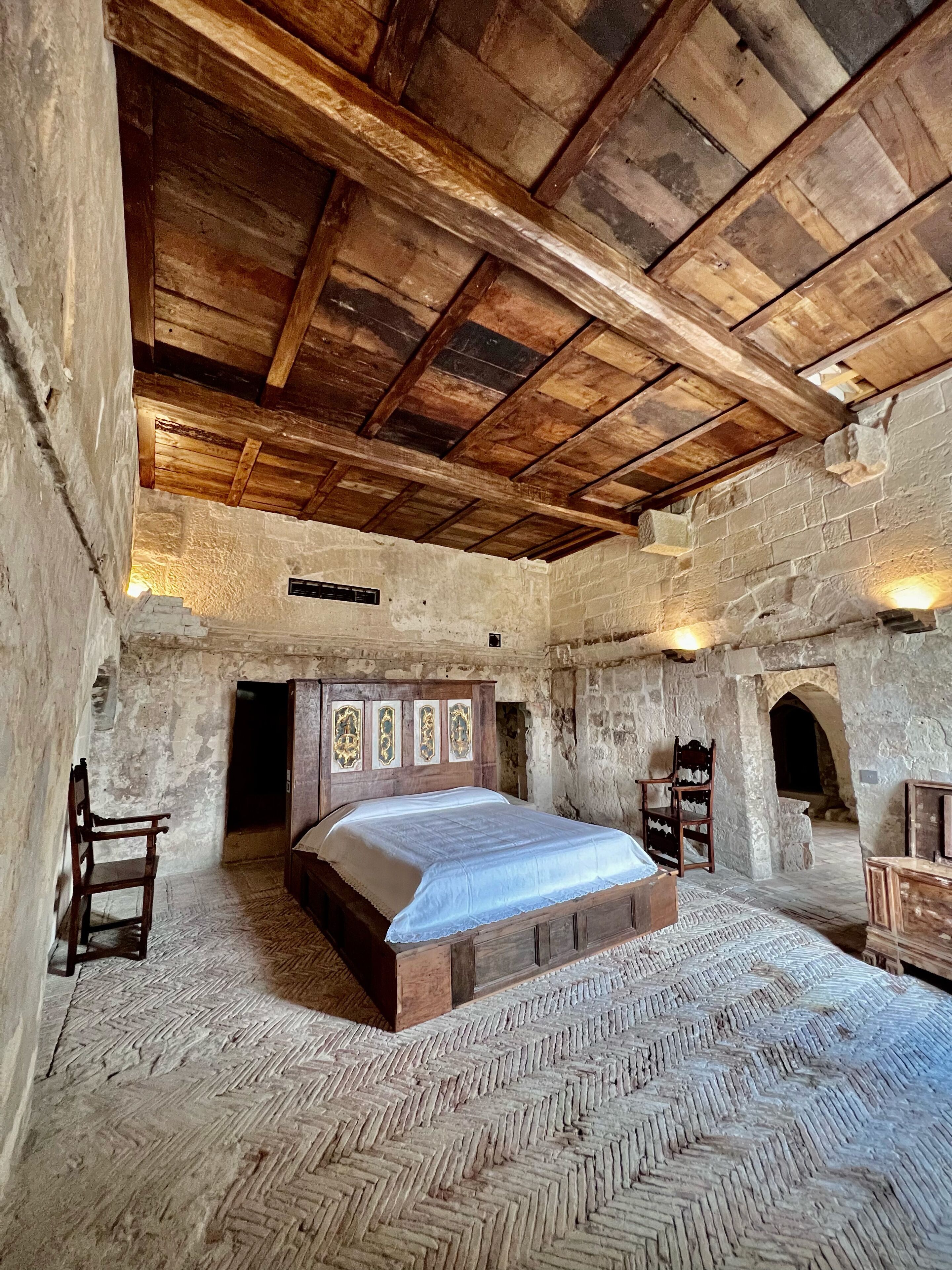 Ein rustikales Schlafzimmer mit einem hölzernen Bett, Steinwänden und einem Fischgrätparkett.