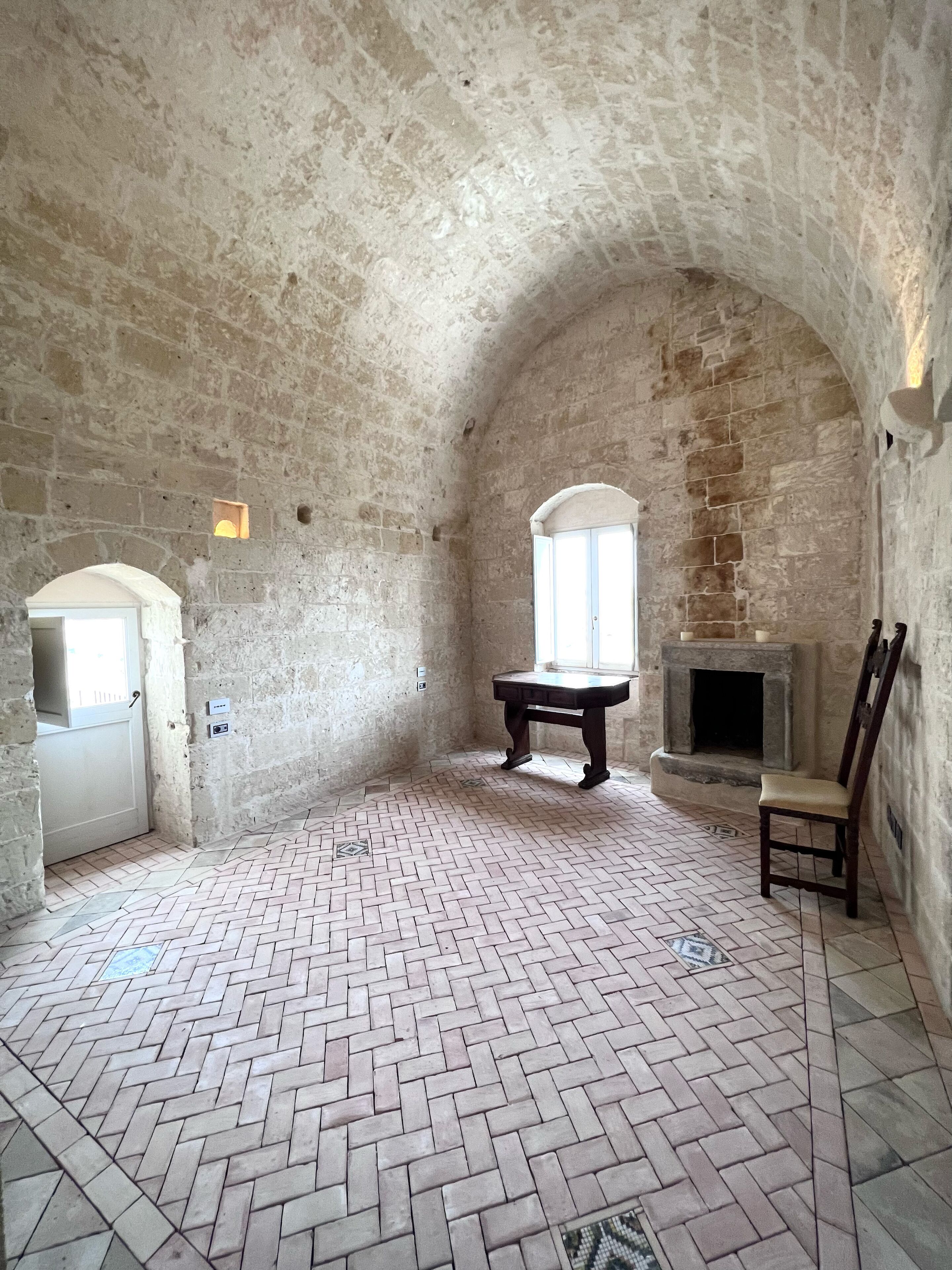 A room with a herringbone floor, stone walls, a fireplace, and a bench.
