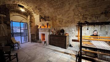 A stone-walled room with a fireplace, a large window, and a loom.