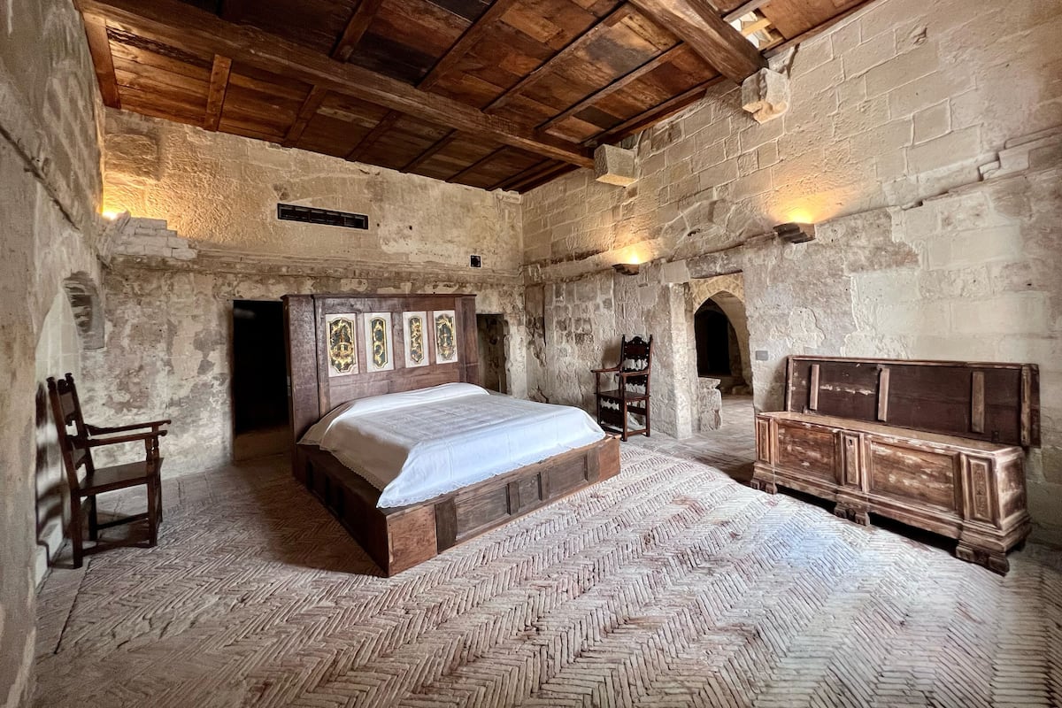 Une chambre à coucher rustique avec un lit en bois, une commode en bois et un mur en pierre.