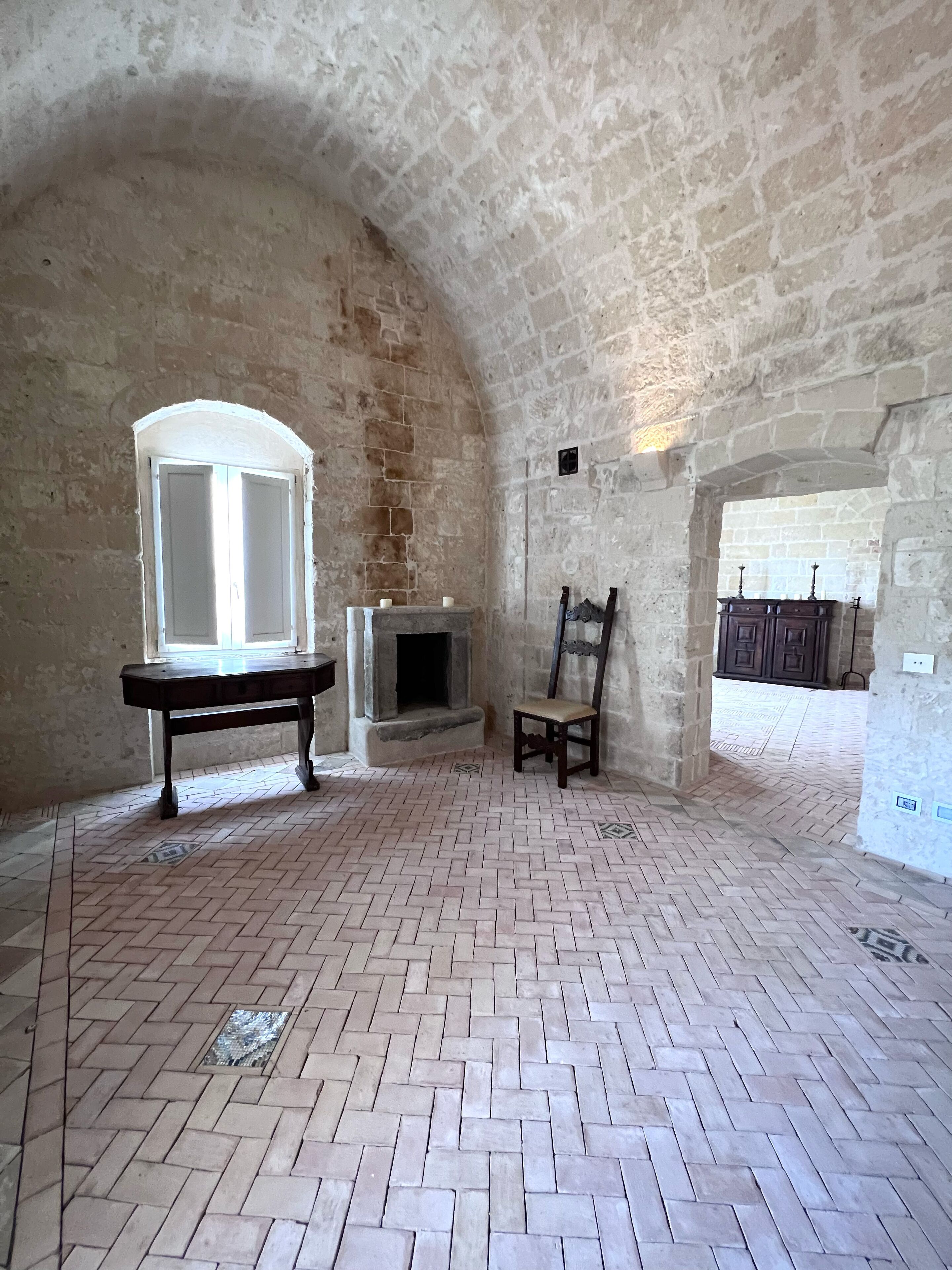 Una stanza con parete in pietra, camino, tavolo di legno e una sedia.