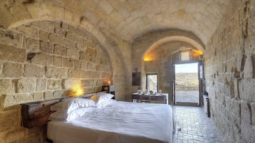 Un dormitorio con paredes de piedra, una cama grande, un cabecero de madera y una mesita con una vela.