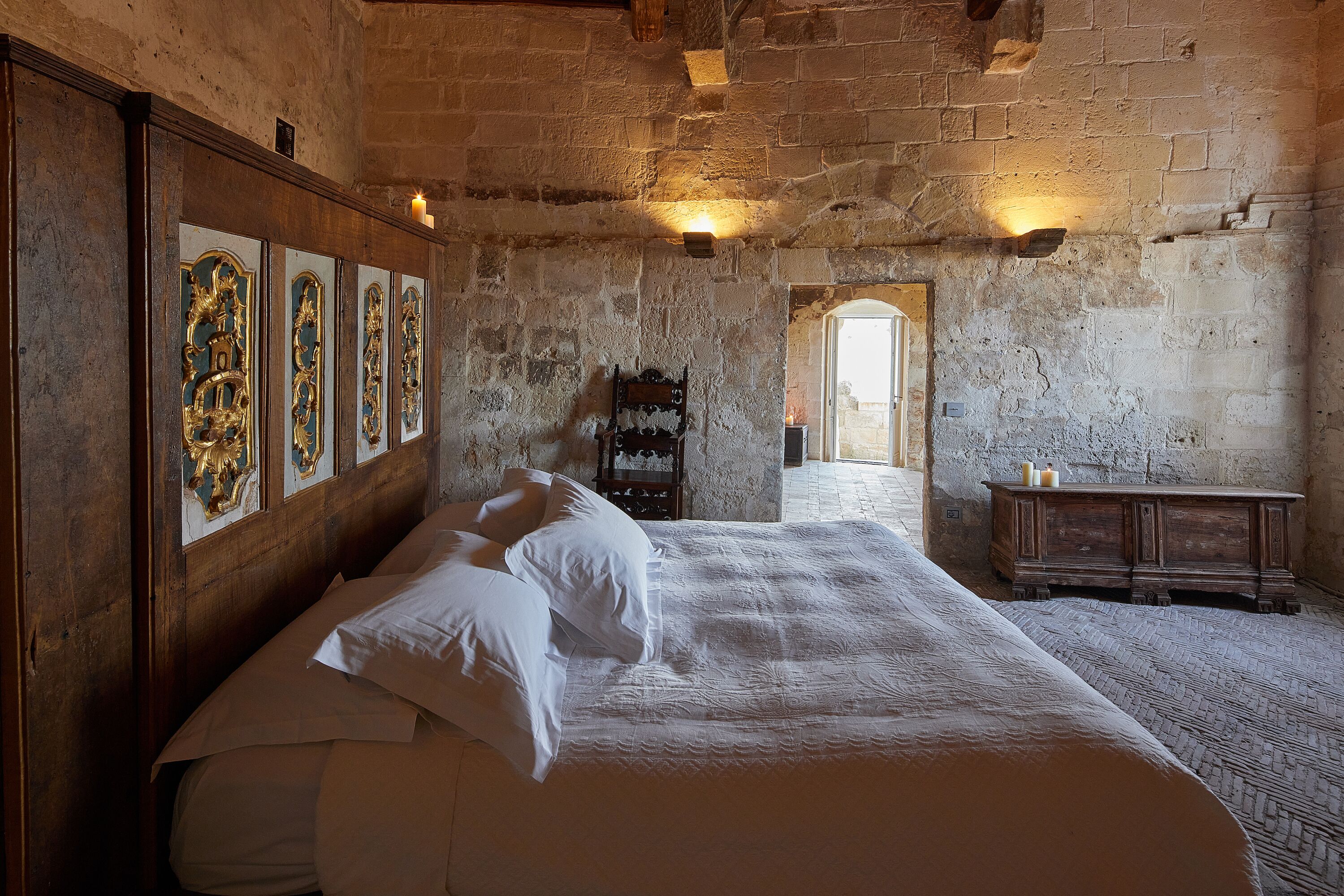 Una stanza con un letto grande, una testiera in legno e un muro in pietra. Si vedono quadri appesi alla parete e un mobile in legno.