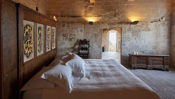 Una stanza con un letto grande, una testiera in legno e un muro in pietra. Si vedono quadri appesi alla parete e un mobile in legno.