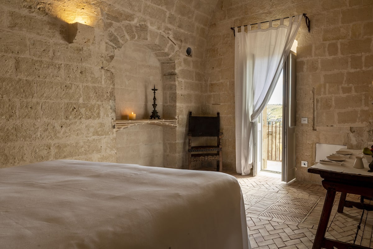 Une pièce aux murs de pierre, avec un lit, une petite table sur laquelle se trouve une bougie et une chaise.