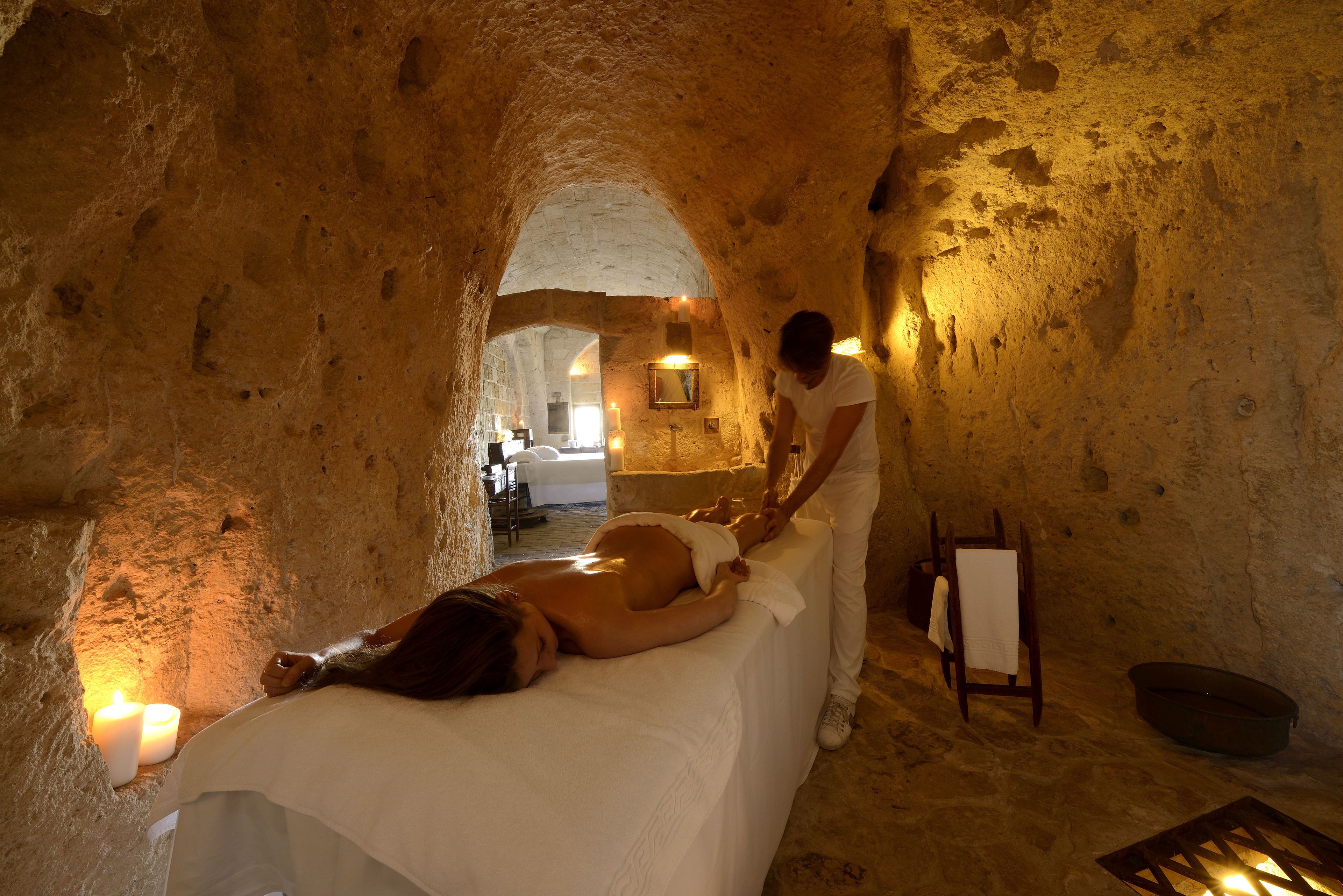 Una stanza spa con lettino da massaggio, candele e una sedia di legno.