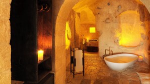 Un baño con paredes de piedra, una bañera grande, un estante con botellas y un perchero para toallas.